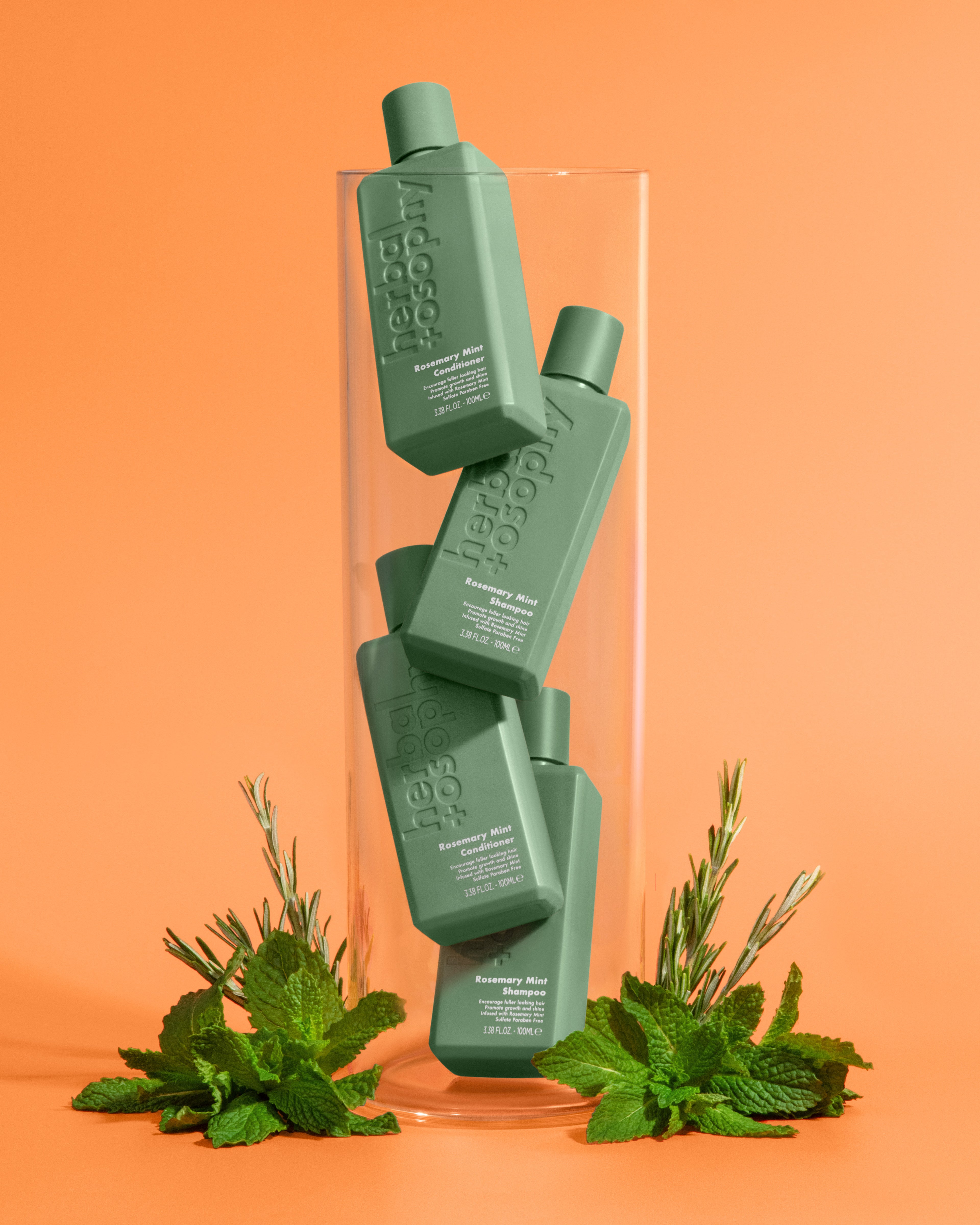 Herbalosophy's rosemary + mint shampoo and conditioners inside a glass tube with rosemary and mint herbs.