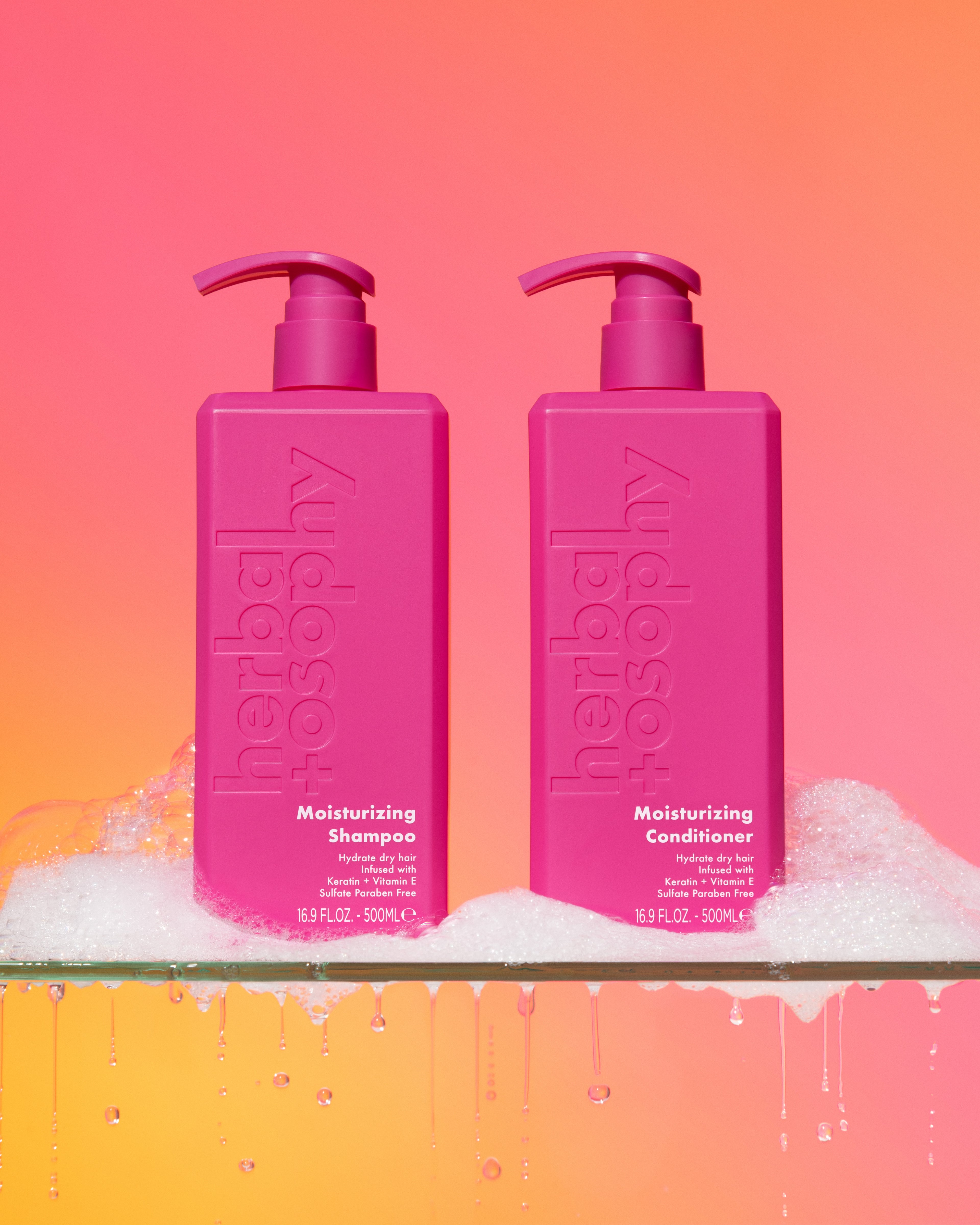 Herbalosophy's moisturizing shampoo and conditioner sitting on a glass shelf