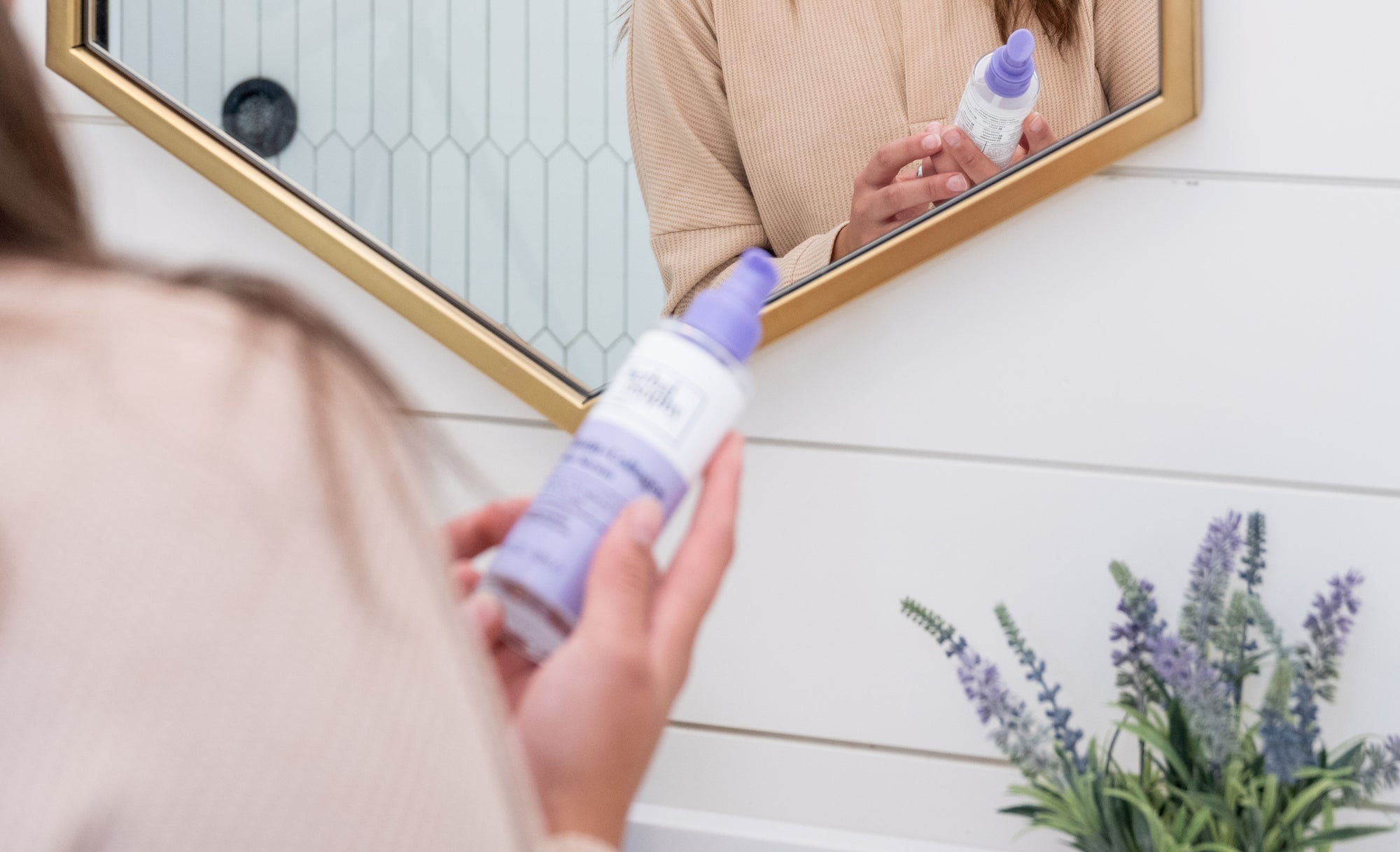 Woman in front of bathroom mirror holding Herbalosophy Biotin + Collagen serum