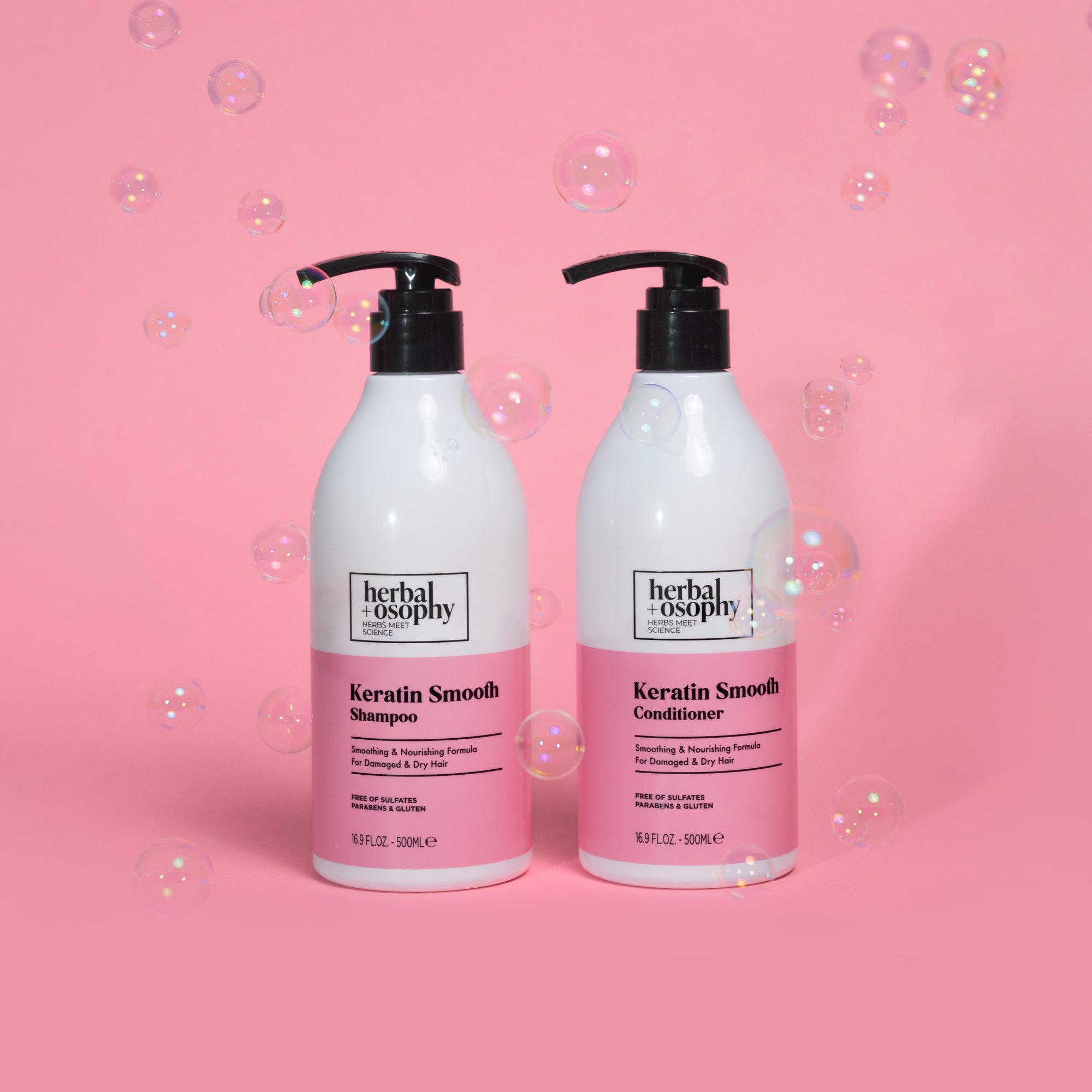 Herbalosophy Keratin Smooth Shampoo and Conditioner bottles on a pink background with bubbles floating around them