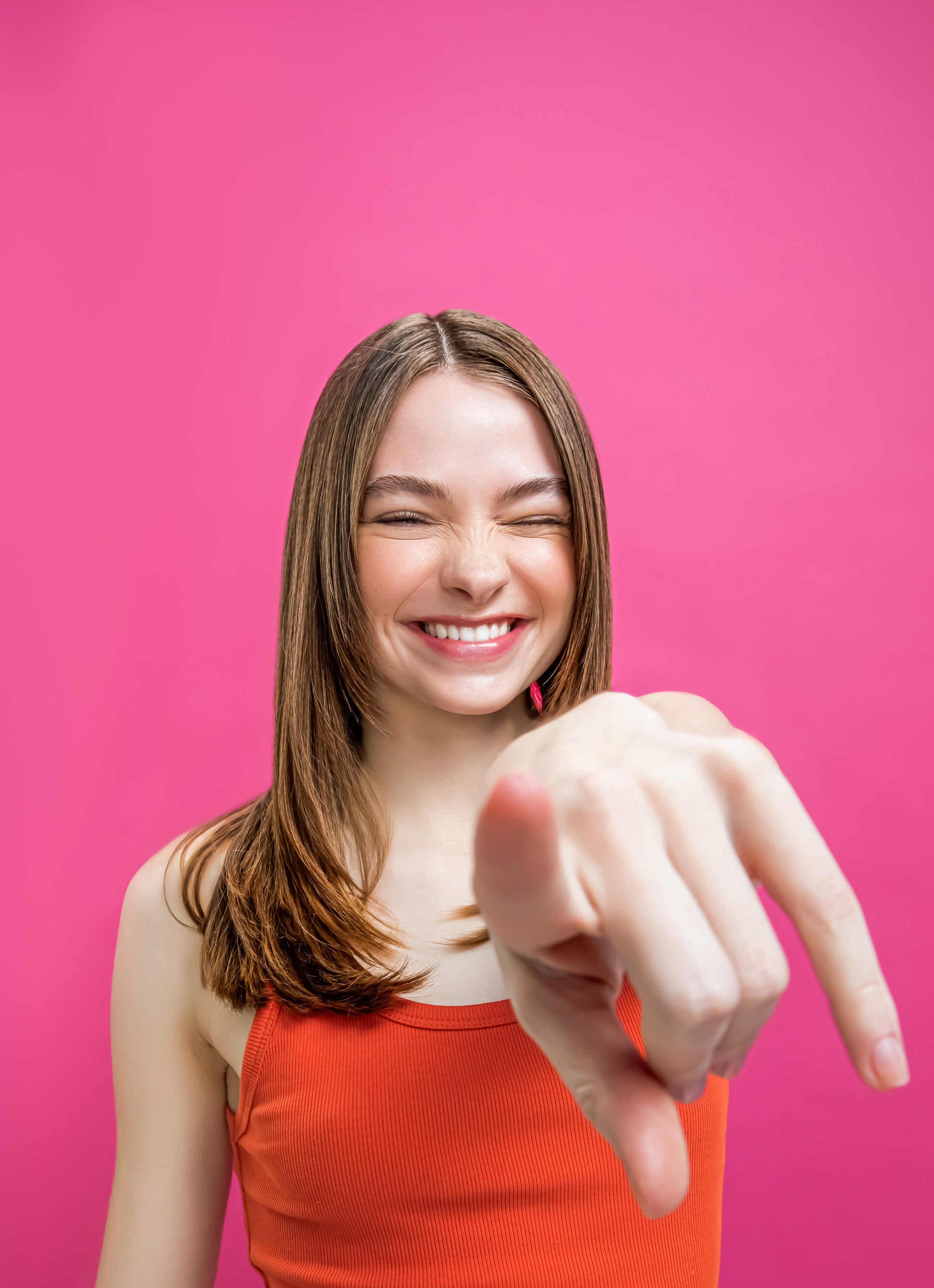 a happy brunette gen z model with stylish hair pointing at the camera.