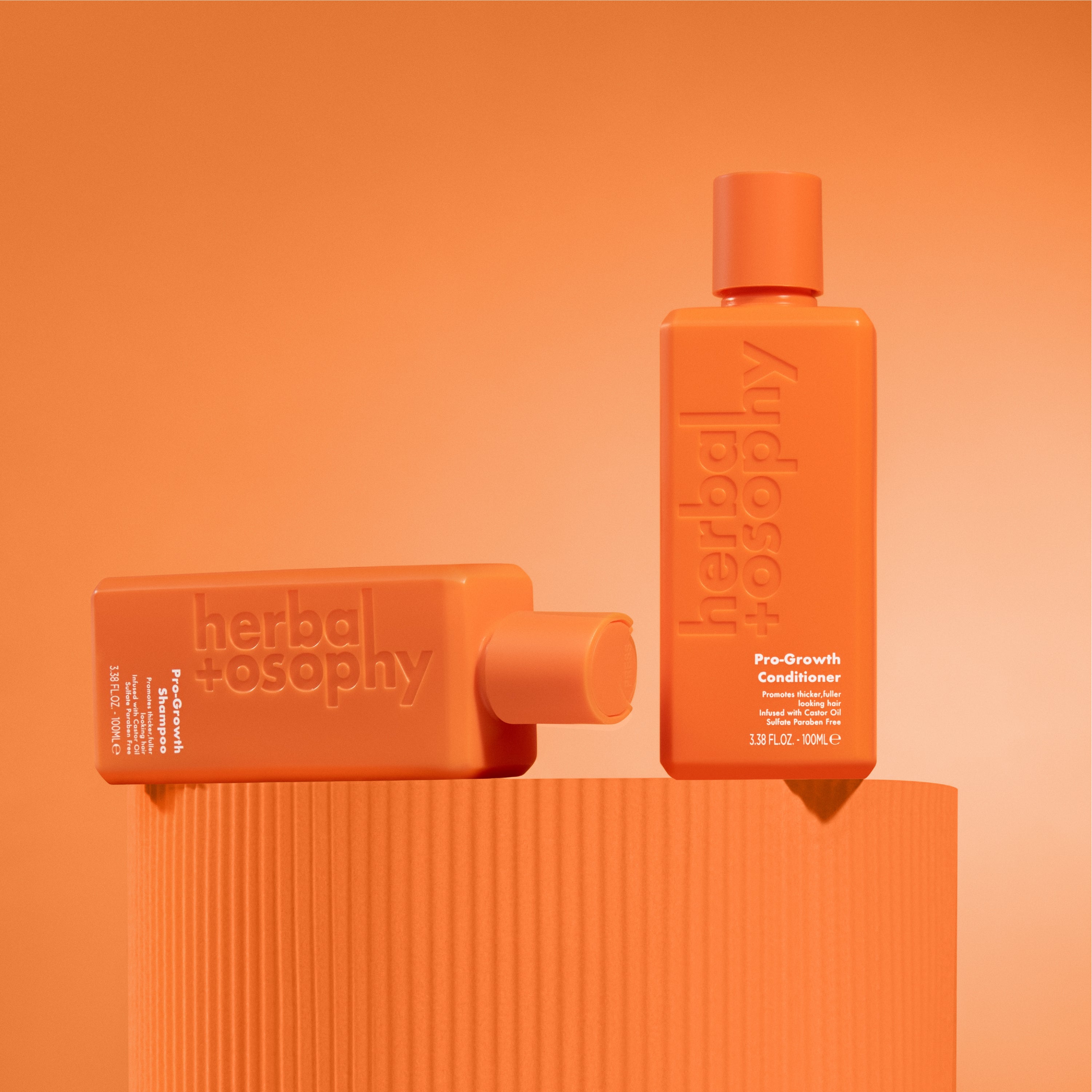 Herbalosophy's pro-growth shampoo and conditioner on a pedestal against an orange background