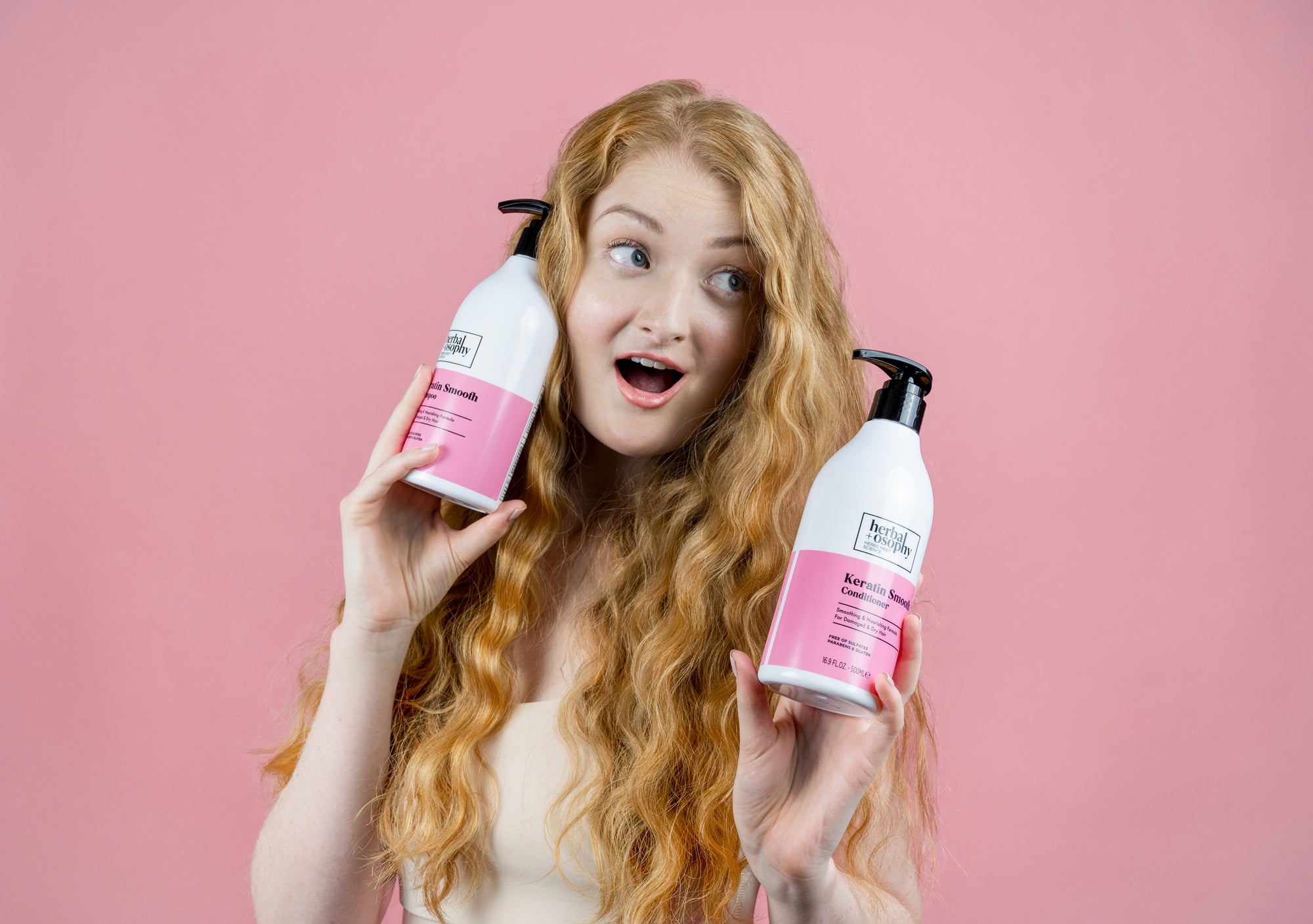woman with long red hair holding Herbalosophy Keratin Smooth shampoo and conditioner bottles