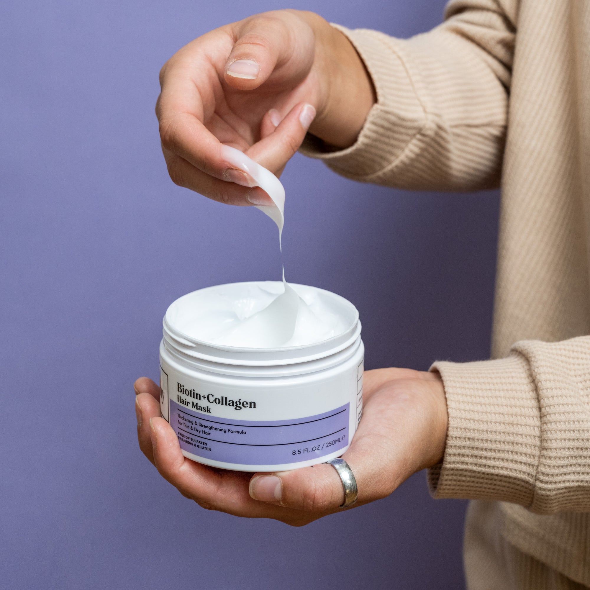 Biotin + Collagen Hair Mask jar held in hand while woman dips hand into cream