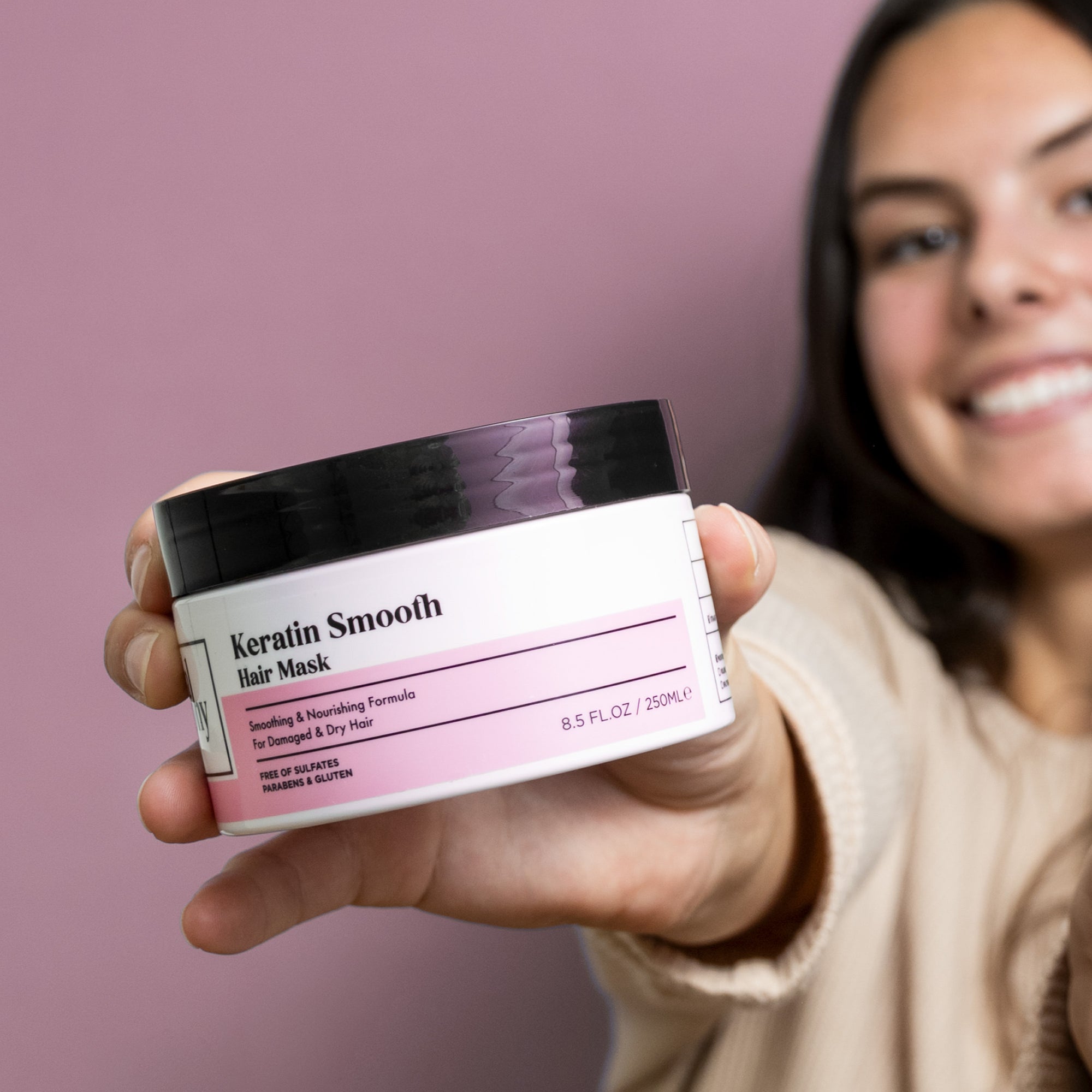 Herbalosophy Keratin Smooth Hair Mask jar held by model toward camera with pink background