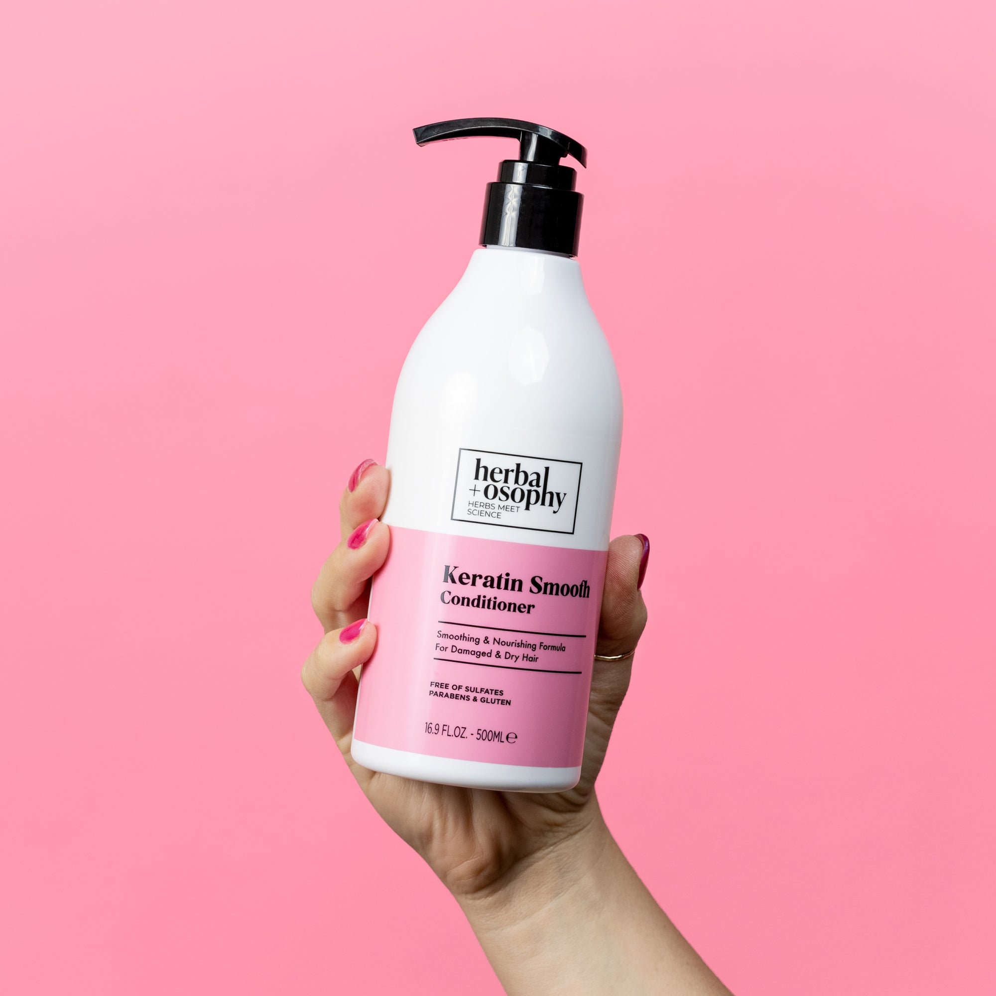Herbalosophy Keratin Smooth Conditioner bottle held in front of pink backdrop