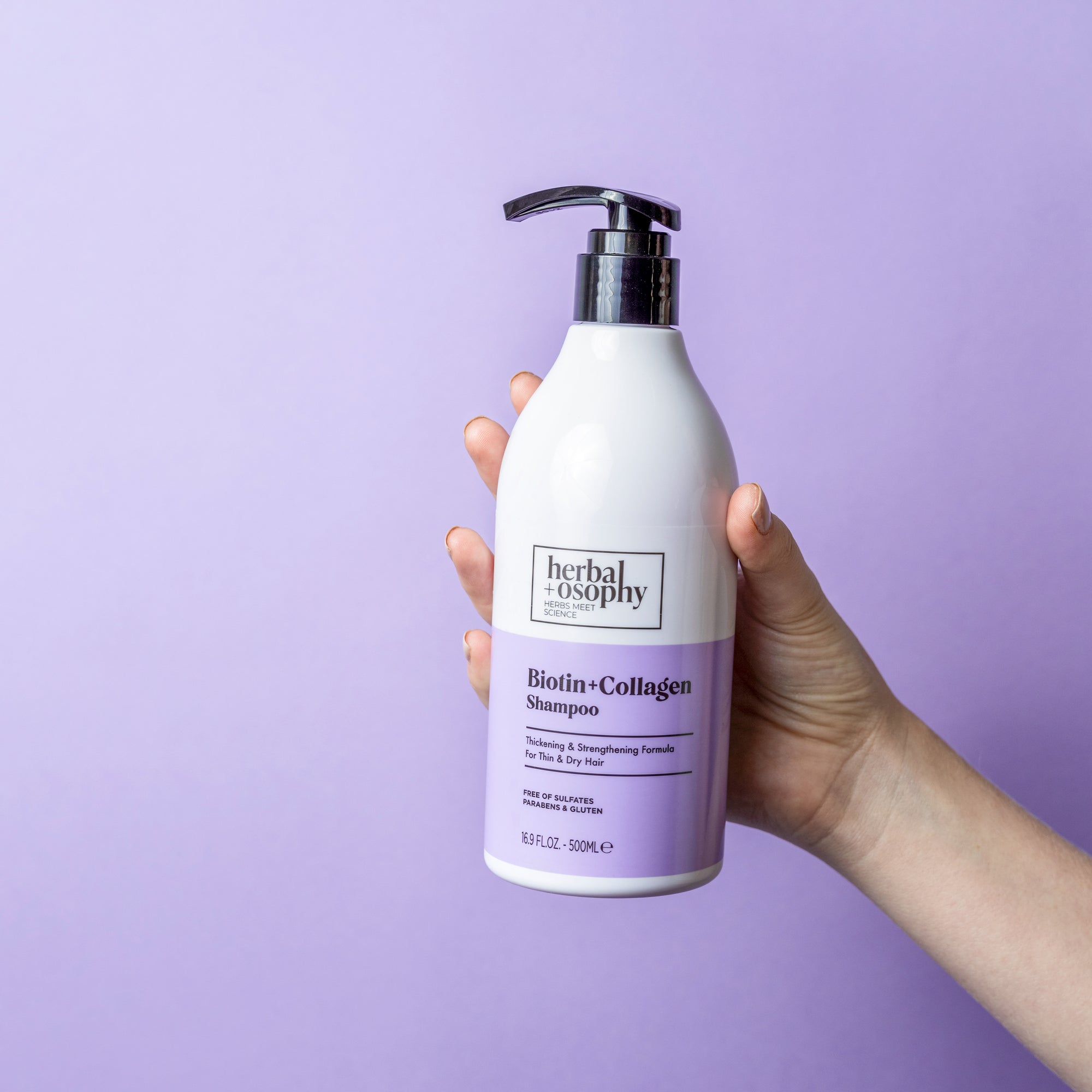 Biotin + Collagen Shampoo bottle held in front of purple backdrop